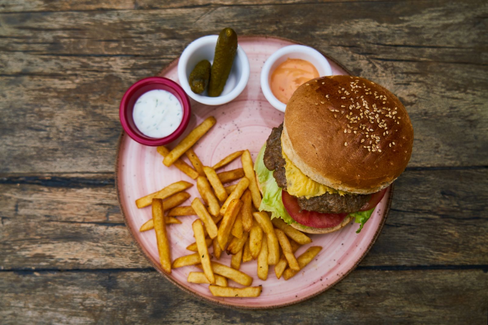 Top view of a tasty cheeseburger served with fries and sauces, perfect for food lovers.