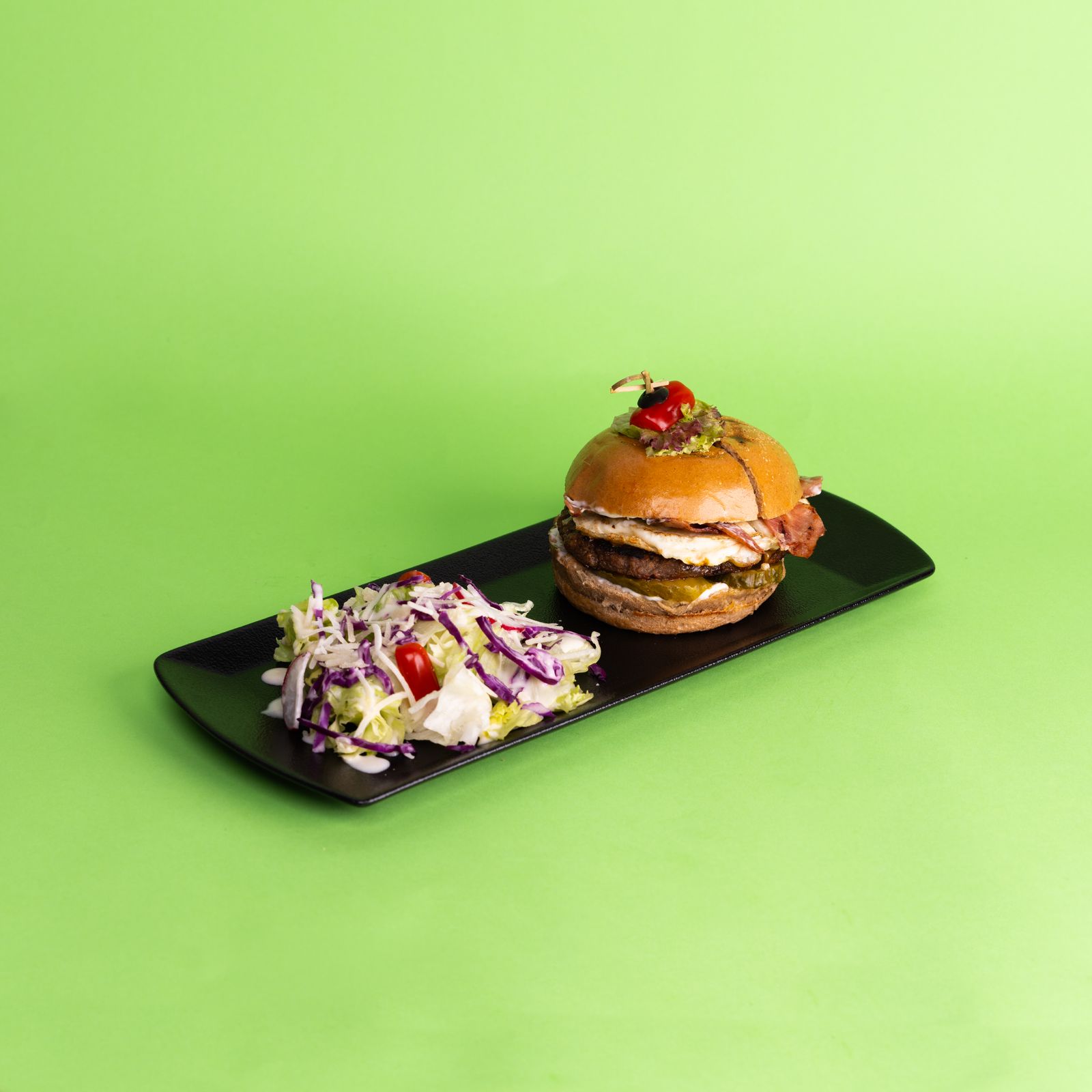Appetizing hamburger served with a fresh salad on a sleek black plate against a green background.