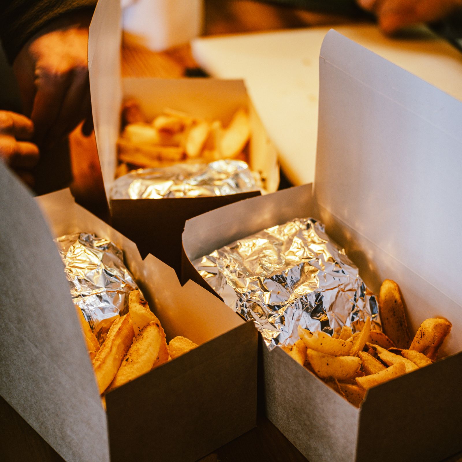 Warm takeout food with fries and foil-wrapped items in cardboard boxes, ready to eat.