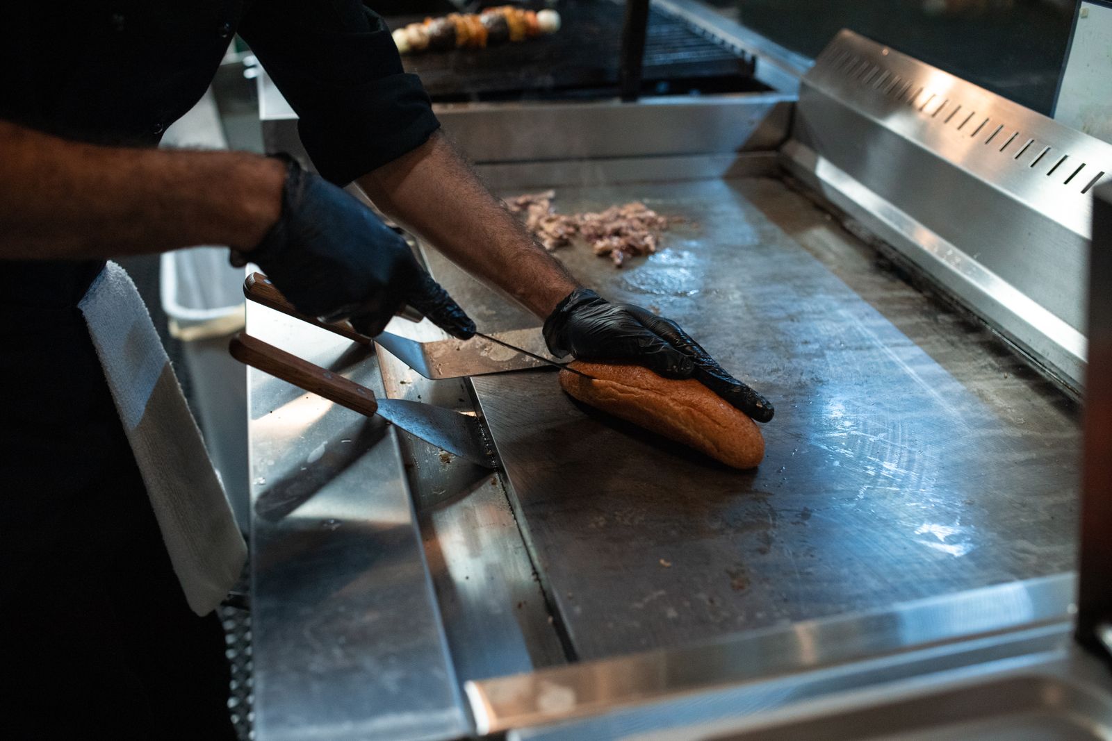 Chef slicing bread on the grill, preparing a sandwich in a professional kitchen setting.